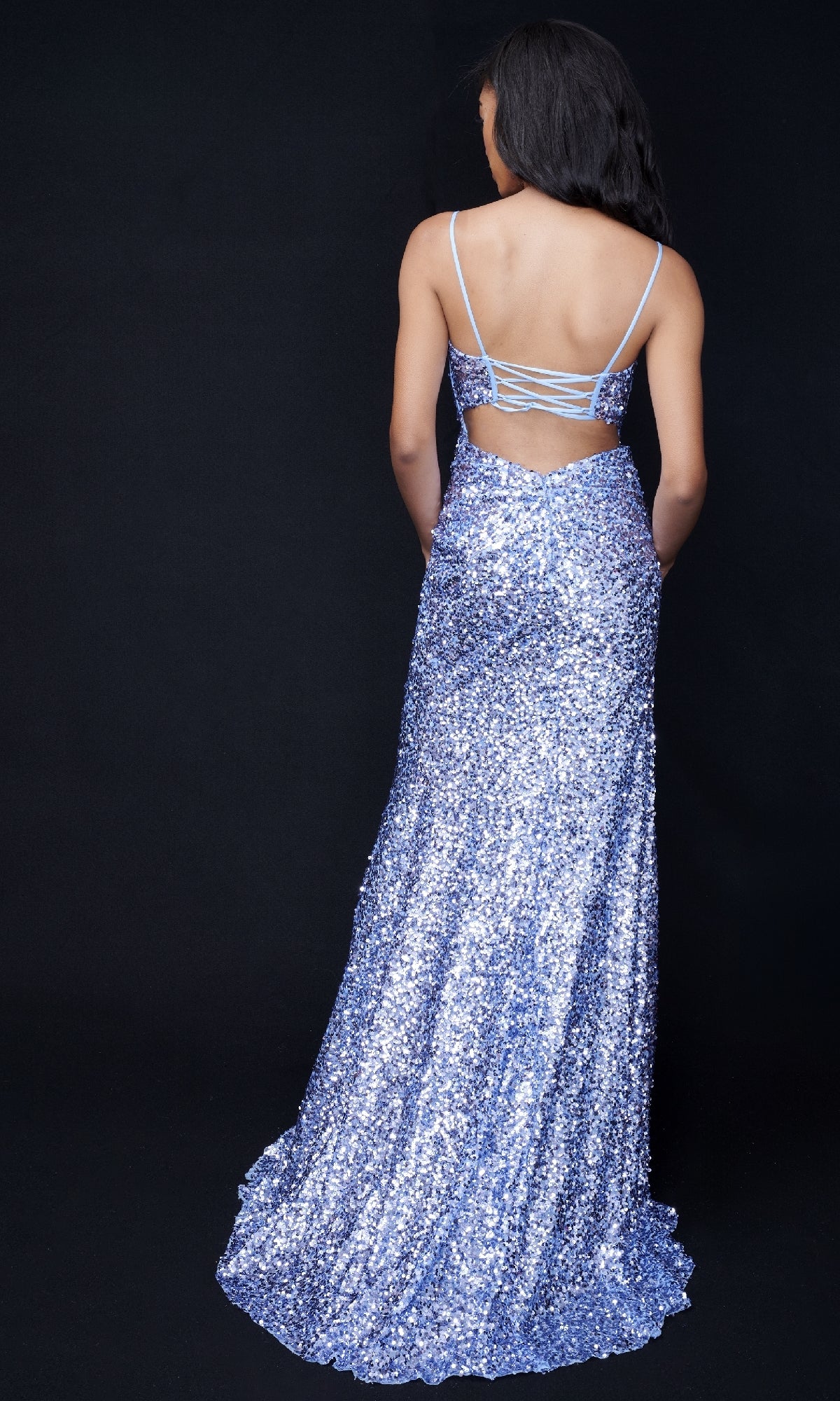 A woman faces away from the camera in the Nina Canacci 4406 Long Sequin Formal Dress, featuring thin straps, a side leg slit, cutout detail, and sparkling silver sequins in a floor-length design.